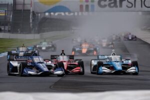 The 2022 IndyCar Series field barrels down into Turn 7 on the Indianapolis Motor Speedway road course.