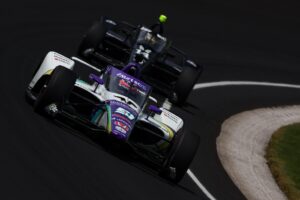 Takuma Sato and Kyle Kirkwood drive through the turn at the Indianapolis Motor Speedway.