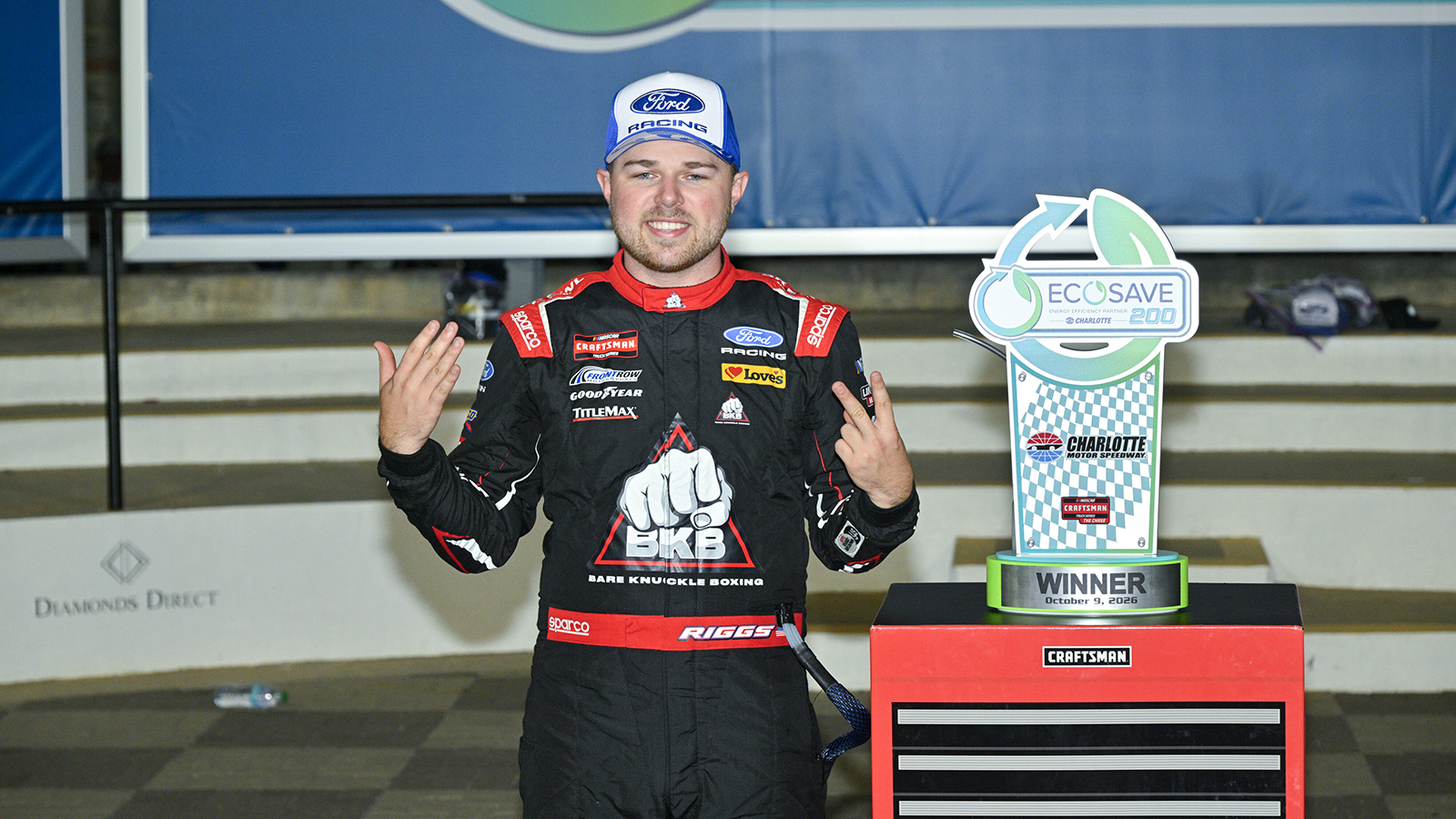 Layne Riggs holds up seven fingers in victory lane at Charlotte Motor Speedway as he celebrates his seventh win of the 2026 season in Friday's Ecosave 200.